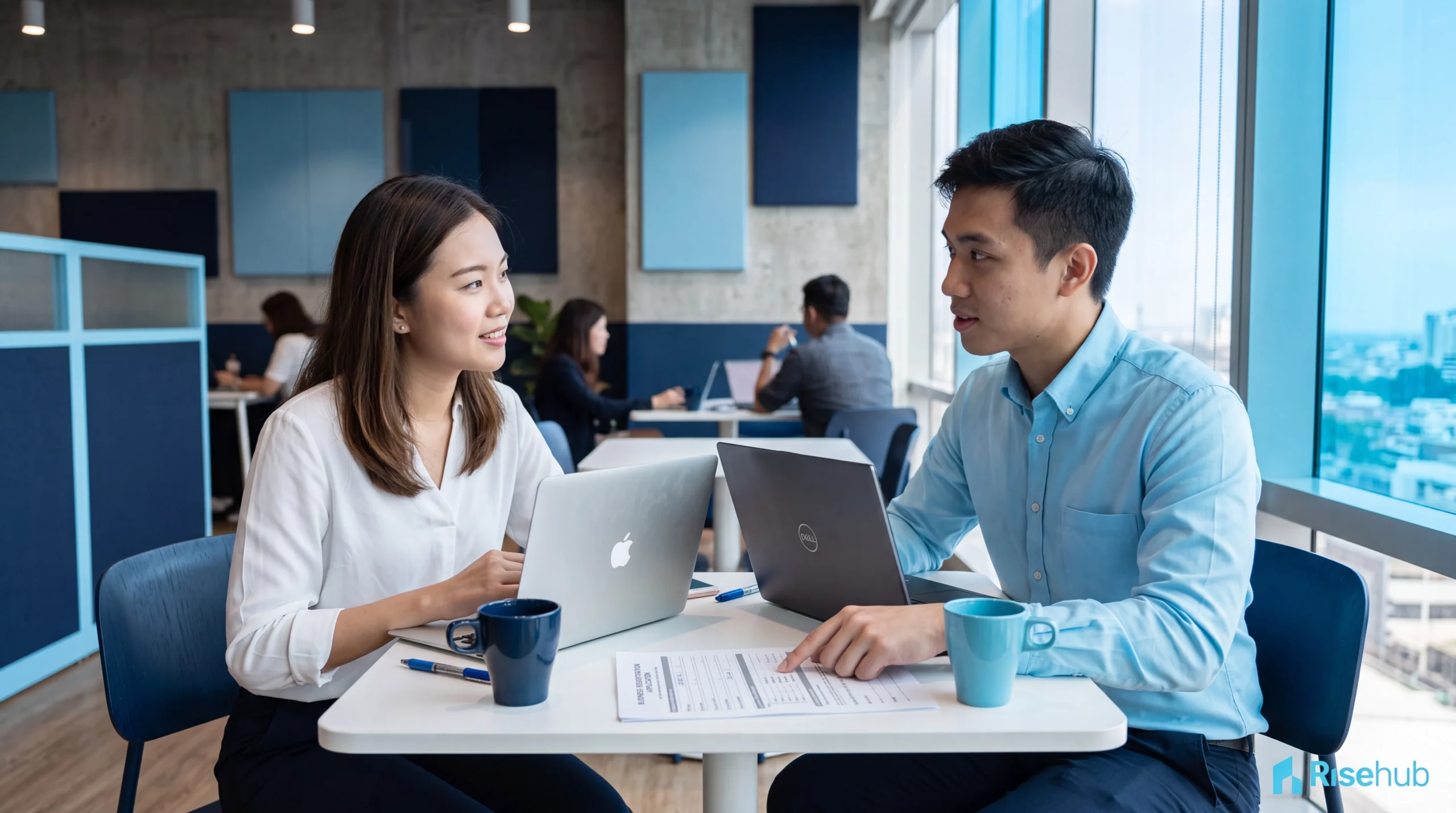 Dua profesional muda Asia berdiskusi sambil meninjau dokumen pendirian PT di meja coworking