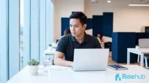 Profesional muda Asia bekerja dari laptop di meja modern — ilustrasi konsep bisnis yang butuh virtual office